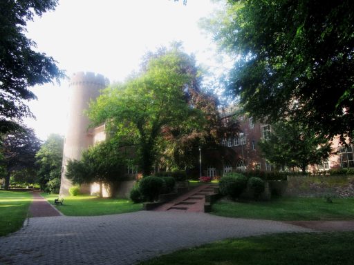 Grüner Park mit Bäumen und einem alten Steingebäude im Hintergrund.